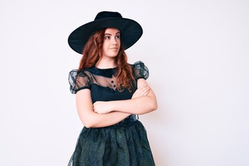 Young beautiful woman wearing witch halloween costume looking to the side with arms crossed convinced and confident