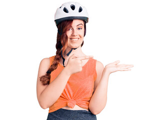 Young beautiful woman wearing bike helmet amazed and smiling to the camera while presenting with hand and pointing with finger.