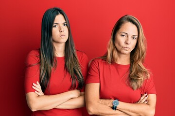 Hispanic family of mother and daughter wearing casual clothes over red background skeptic and nervous, disapproving expression on face with crossed arms. negative person.