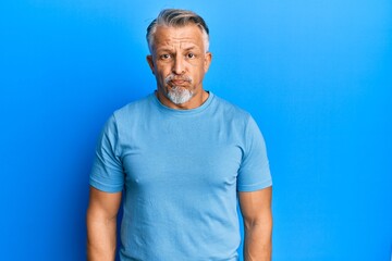 Middle age grey-haired man wearing casual clothes puffing cheeks with funny face. mouth inflated with air, crazy expression.