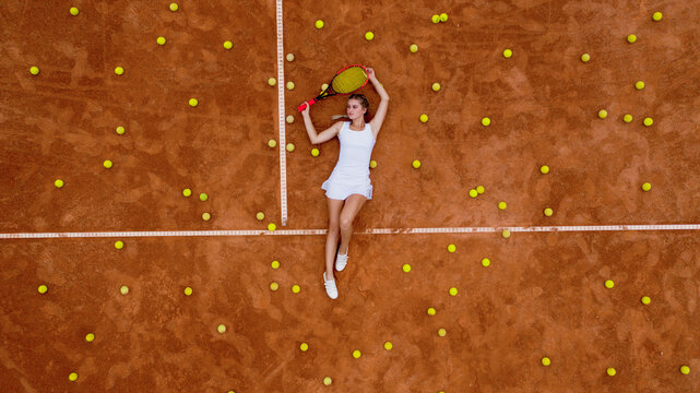Portrait of smiling woman relaxing on tennis court with a lot of balls and racket after hard tennis trainingg outdoor. Dolly shot. Top view