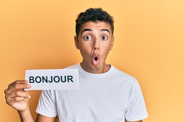 Young handsome african american man holding bonjour french greeting word scared and amazed with open mouth for surprise, disbelief face © Krakenimages.com