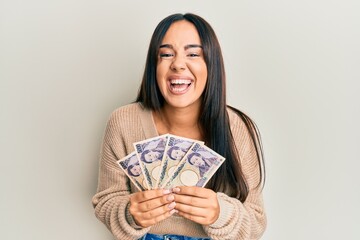 Young beautiful hispanic girl holding japanese yen banknotes smiling and laughing hard out loud because funny crazy joke.