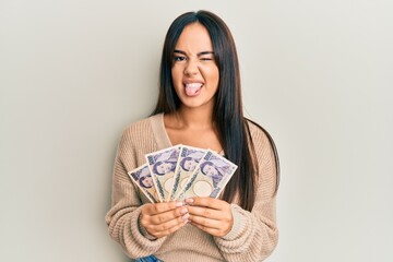 Young beautiful hispanic girl holding japanese yen banknotes sticking tongue out happy with funny expression.
