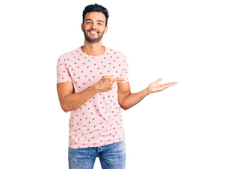 Young handsome hispanic man wearing casual clothes amazed and smiling to the camera while presenting with hand and pointing with finger.