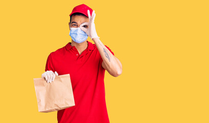 Young handsome hispanic man delivering food wearing covid-19 safety mask smiling happy doing ok sign with hand on eye looking through fingers