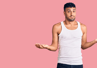 Young hispanic man wearing casual clothes clueless and confused expression with arms and hands raised. doubt concept.