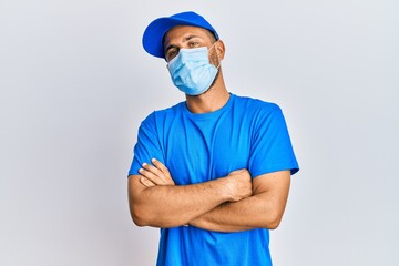 Handsome man with beard wearing courier uniform and medical mask happy face smiling with crossed arms looking at the camera. positive person.