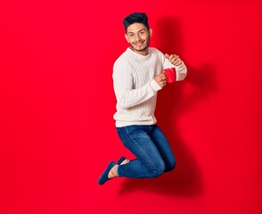 Young handsome latin man smiling happy drinking cup of coffee. Jumping with smile on face over...