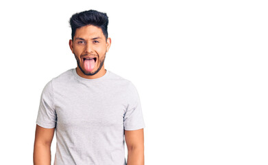 Handsome latin american young man wearing casual tshirt sticking tongue out happy with funny expression. emotion concept.