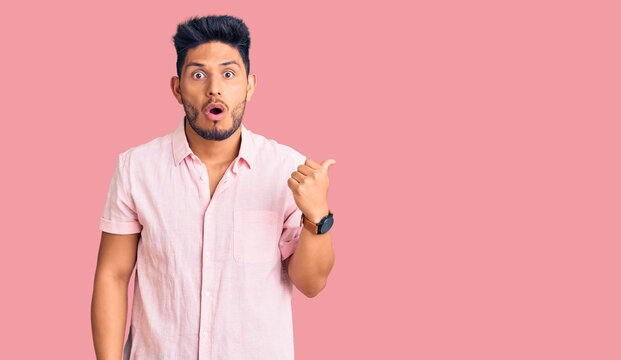 Handsome latin american young man wearing casual summer shirt surprised pointing with hand finger to the side, open mouth amazed expression.