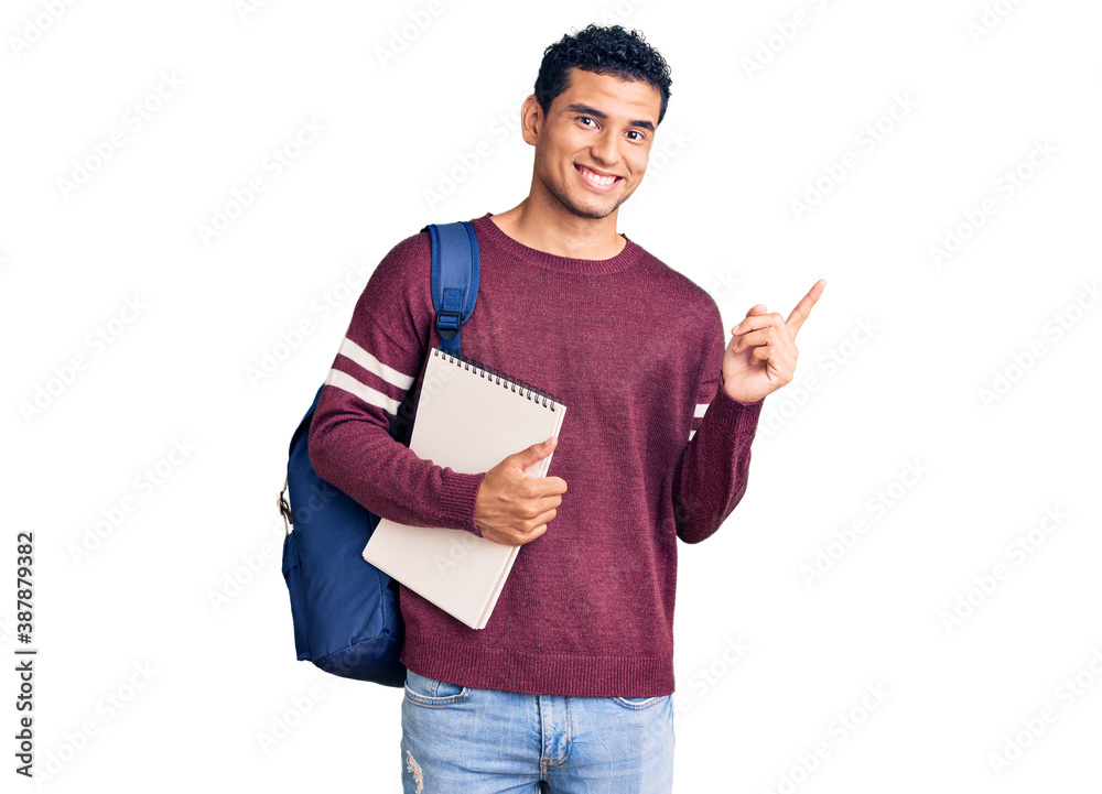 Wall mural hispanic handsome young man wearing student backpack and notebook smiling happy pointing with hand a