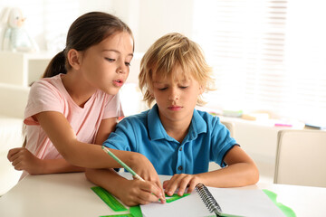 Little boy and girl doing homework at table indoors