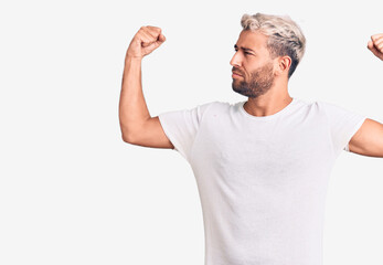 Young handsome blond man wearing casual t-shirt showing arms muscles smiling proud. fitness concept.