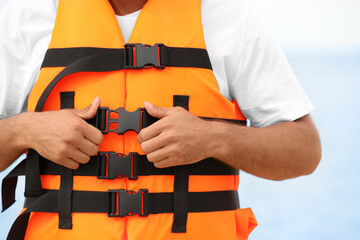 Male lifeguard putting on life vest near sea, closeup
