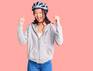 Young beautiful chinese girl wearing bike helmet screaming proud, celebrating victory and success very excited with raised arms