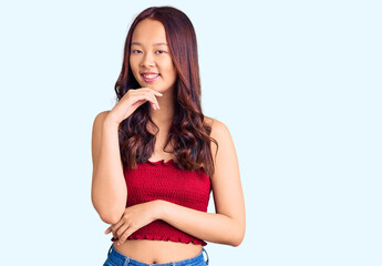 Young beautiful chinese girl wearing casual clothes looking confident at the camera with smile with crossed arms and hand raised on chin. thinking positive.