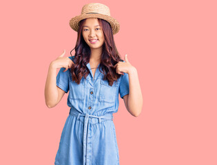 Young beautiful chinese girl wearing summer hat looking confident with smile on face, pointing oneself with fingers proud and happy.