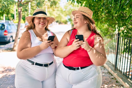 Two plus size overweight sisters twins women with smartphone outdoors on a sunny day