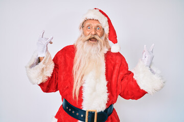 Old senior man with grey hair and long beard wearing santa claus costume with suspenders shouting with crazy expression doing rock symbol with hands up. music star. heavy concept.