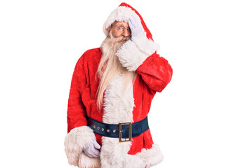 Old senior man with grey hair and long beard wearing traditional santa claus costume covering one eye with hand, confident smile on face and surprise emotion.