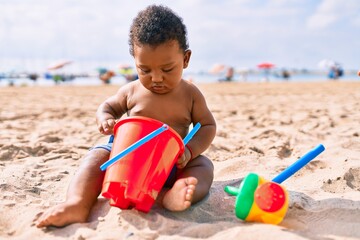 Adorable african american toddler playing with toys sitting on the sand at the beach.