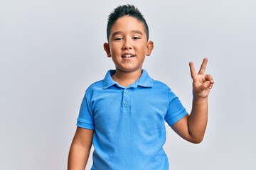 Little boy hispanic kid wearing casual clothes smiling with happy face winking at the camera doing victory sign. number two.