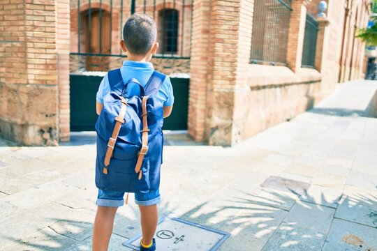 Adorable student boy on back view wearing backpack at street of city.