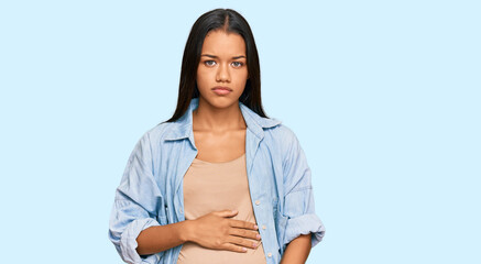 Beautiful hispanic woman expecting a baby showing pregnant belly with serious expression on face. simple and natural looking at the camera.