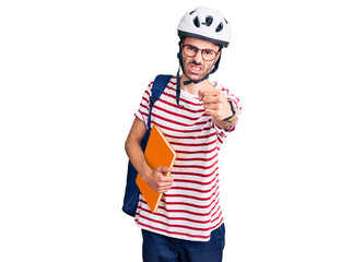 Young hispanic man wearing student backpack and bike helmet holding binder annoyed and frustrated shouting with anger, yelling crazy with anger and hand raised