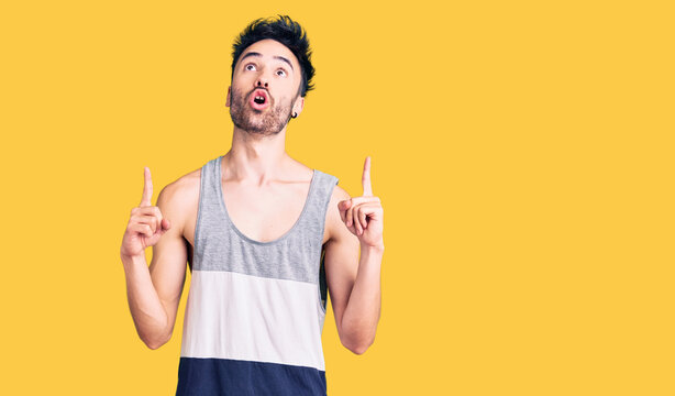 Young hispanic man wearing casual clothes amazed and surprised looking up and pointing with fingers and raised arms.