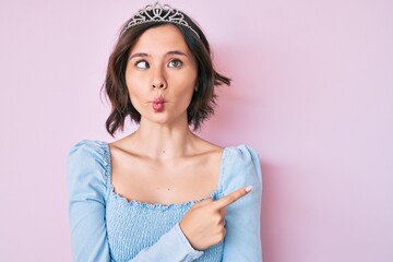 Young beautiful girl wearing princess crown making fish face with mouth and squinting eyes, crazy and comical. © Krakenimages.com