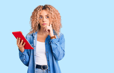 Young blonde woman with curly hair using touchpad device serious face thinking about question with...