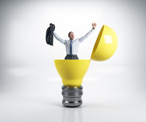 Happy businessman sitting in a big yellow light bulb.