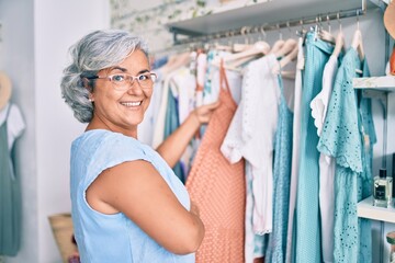 Middle age woman with grey hair at retail shop smiling happy looking at clothes