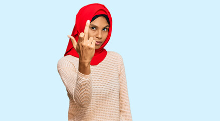 Young african american woman wearing traditional islamic hijab scarf showing middle finger, impolite and rude fuck off expression