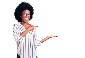 Young african american woman wearing casual clothes and glasses amazed and smiling to the camera while presenting with hand and pointing with finger.