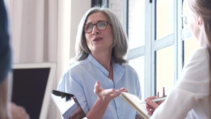 Mature older female mentor coach training young interns at group office meeting professional workshop. Senior business woman teacher professor leader working with students at seminar education class.