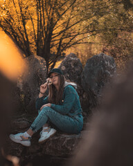 Portrait of an attractive brunette sitting in a stone well at the Rajcica wells landmark. Wearing jeans pants, jacket and a black cap, holding a bouquet of handpicked flowers on a cold autumn day