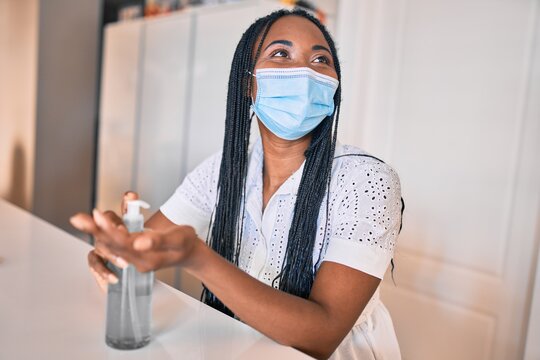 Young african american woman wearing medical mask using sanitizer hand gel at home