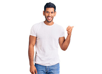 Young latin man wearing casual clothes smiling with happy face looking and pointing to the side with thumb up.