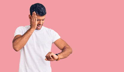 Young latin man wearing casual clothes looking at the watch time worried, afraid of getting late