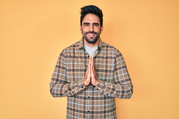 Handsome hispanic man with beard wearing casual clothes praying with hands together asking for forgiveness smiling confident.