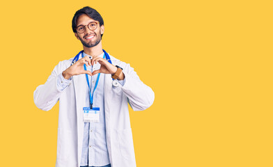 Handsome hispanic man wearing doctor uniform and stethoscope smiling in love showing heart symbol...