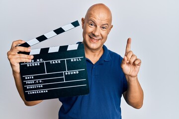 Middle age bald man holding video film clapboard smiling with an idea or question pointing finger...