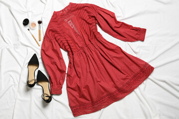 Flat lay composition with stylish red dress on white fabric