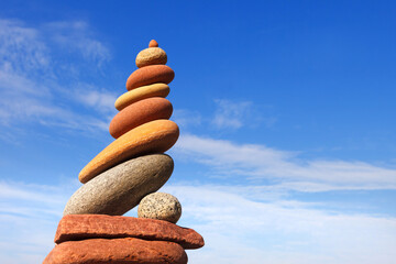 Fototapeta na wymiar Rock zen pyramid of red and yellow pebbles on a background of blue sky and sea.