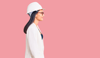 Young beautiful latin girl wearing architect hardhat and glasses looking to side, relax profile pose with natural face with confident smile.