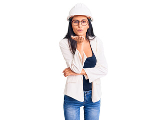 Young beautiful latin girl wearing architect hardhat and glasses looking at the camera blowing a kiss with hand on air being lovely and sexy. love expression.