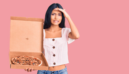 Young beautiful latin girl holding delivery pizza box stressed and frustrated with hand on head, surprised and angry face